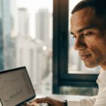 Pessoa analisando gráficos financeiros em celular e notebook, para o artigo B3: Guia Completo da Bolsa do Brasil – O que é...