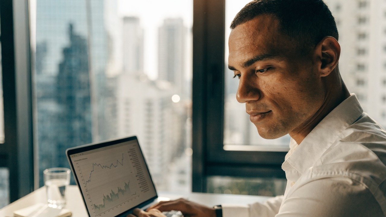 Pessoa analisando gráficos financeiros em celular e notebook, para o artigo B3: Guia Completo da Bolsa do Brasil – O que é...