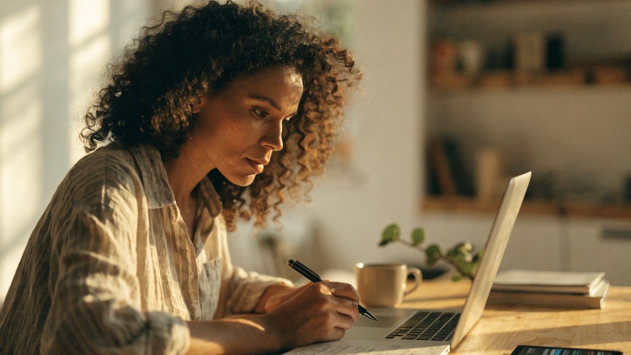 Pessoa analisando gráficos financeiros em celular e notebook, para o artigo Como conseguir dinheiro extra: 20 ideias práti...