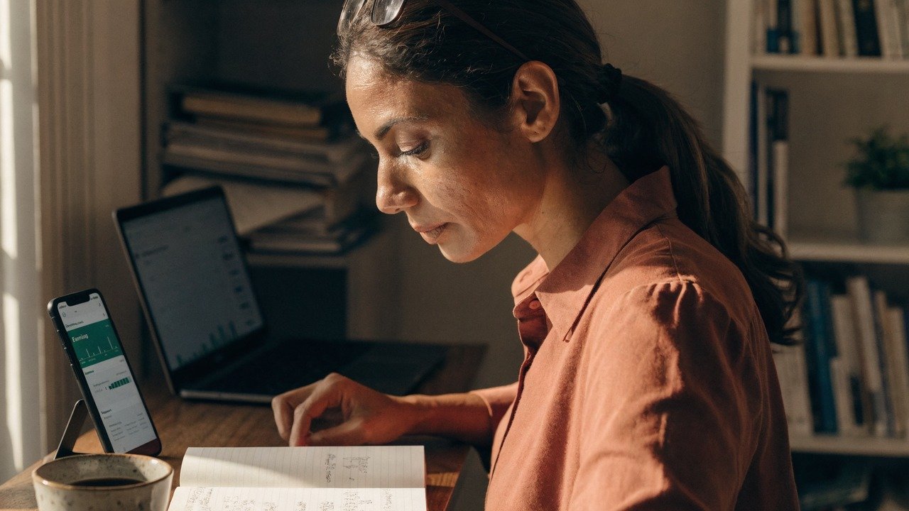 Pessoa analisando gráficos financeiros em celular e notebook, para o artigo Como conseguir uma renda extra: Guia prático d...