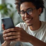 Pessoa brasileira trabalhando em ambiente digital profissional usando o celular e produtos organizados para ilustrar Como ser afiliado do.